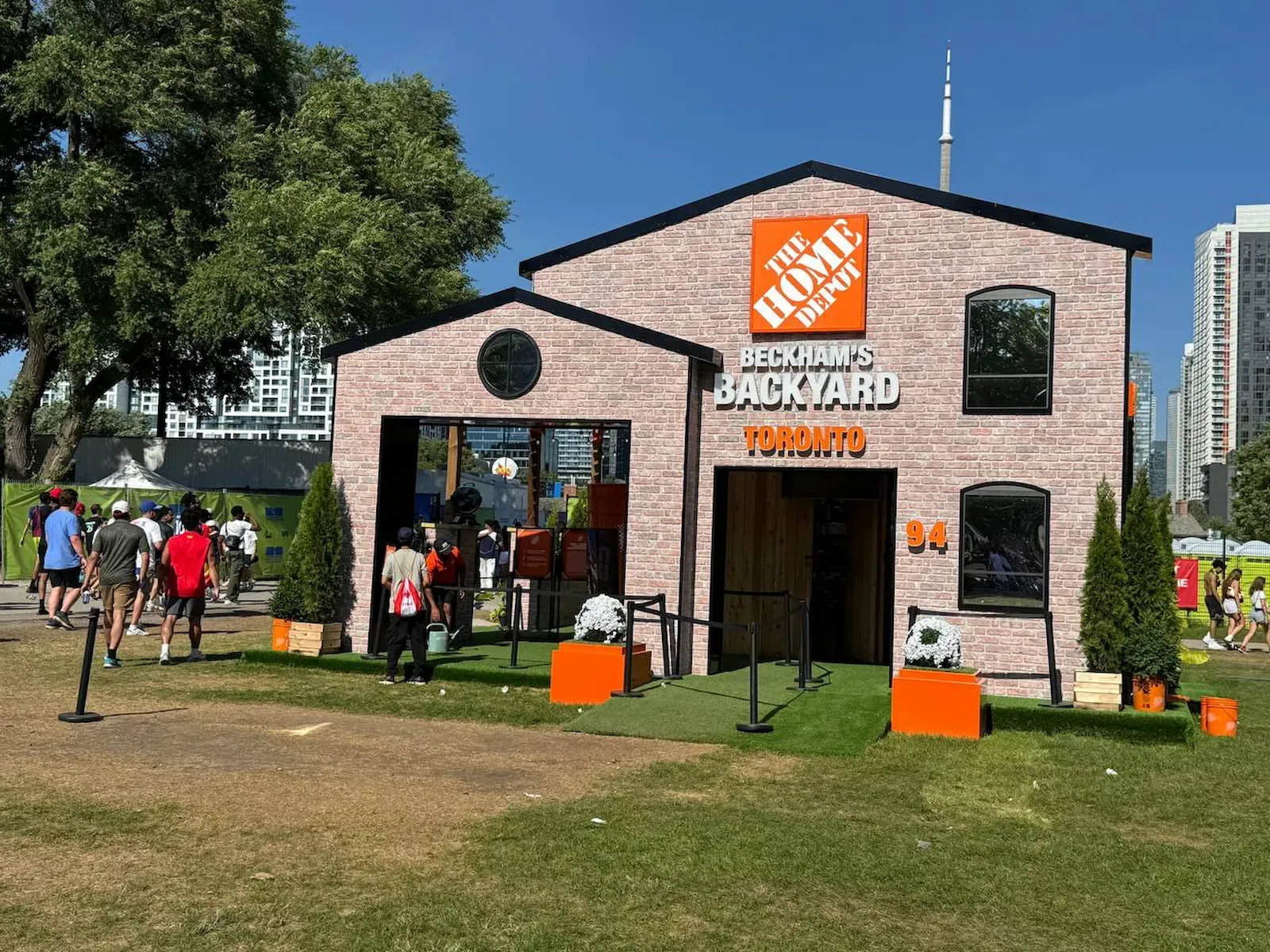 Black belt posts marking the approach to a branded Home Depot activation structure on a festival site, the CN Tower behind it