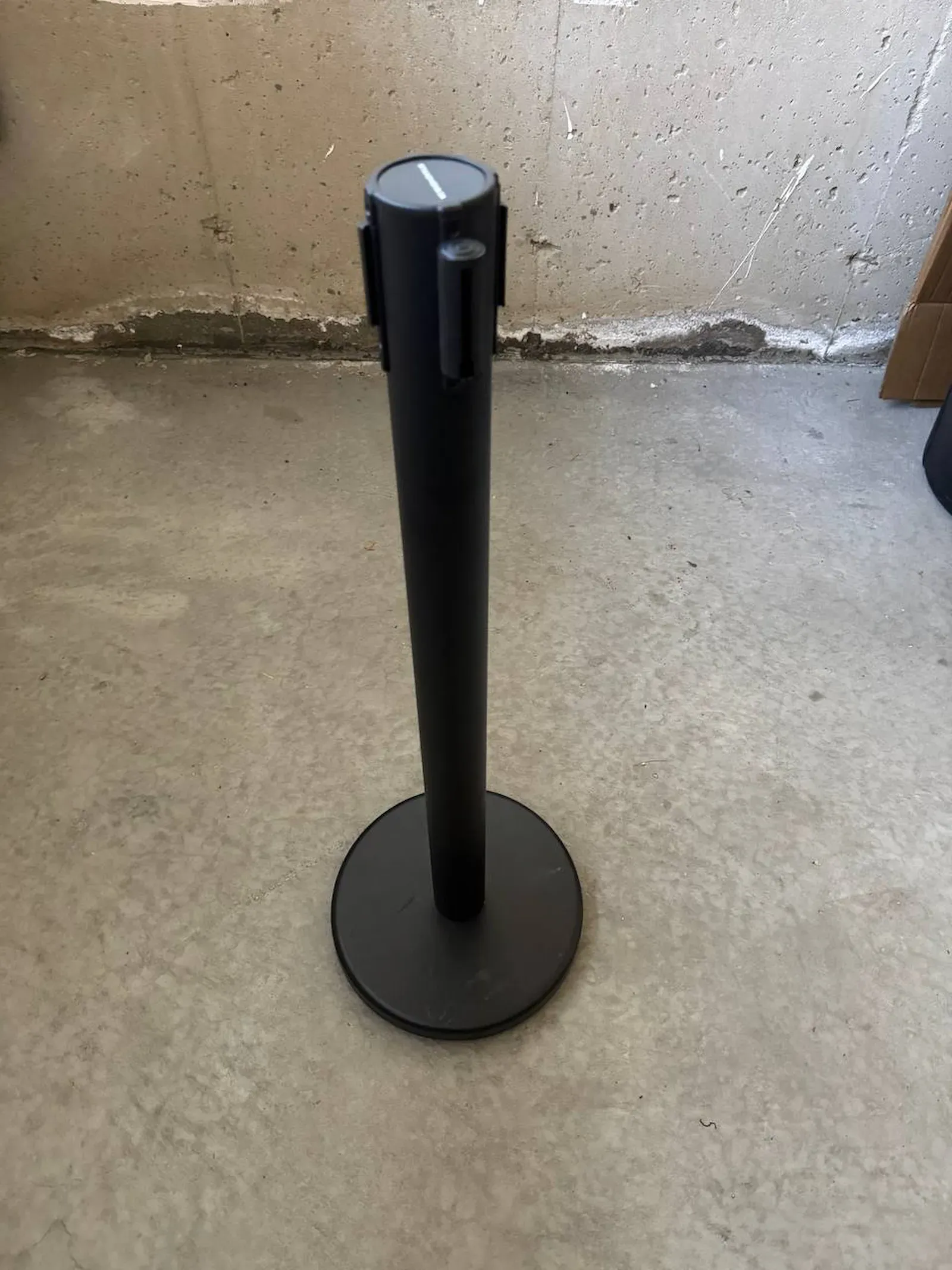 A single black post photographed against a concrete wall, showing the belt cassette and the four receiver slots around the head