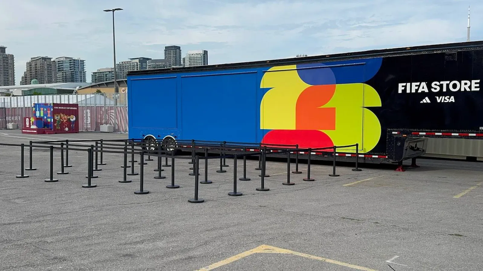 A switchback queue built from black belt posts in front of a merchandise trailer in a stadium car park