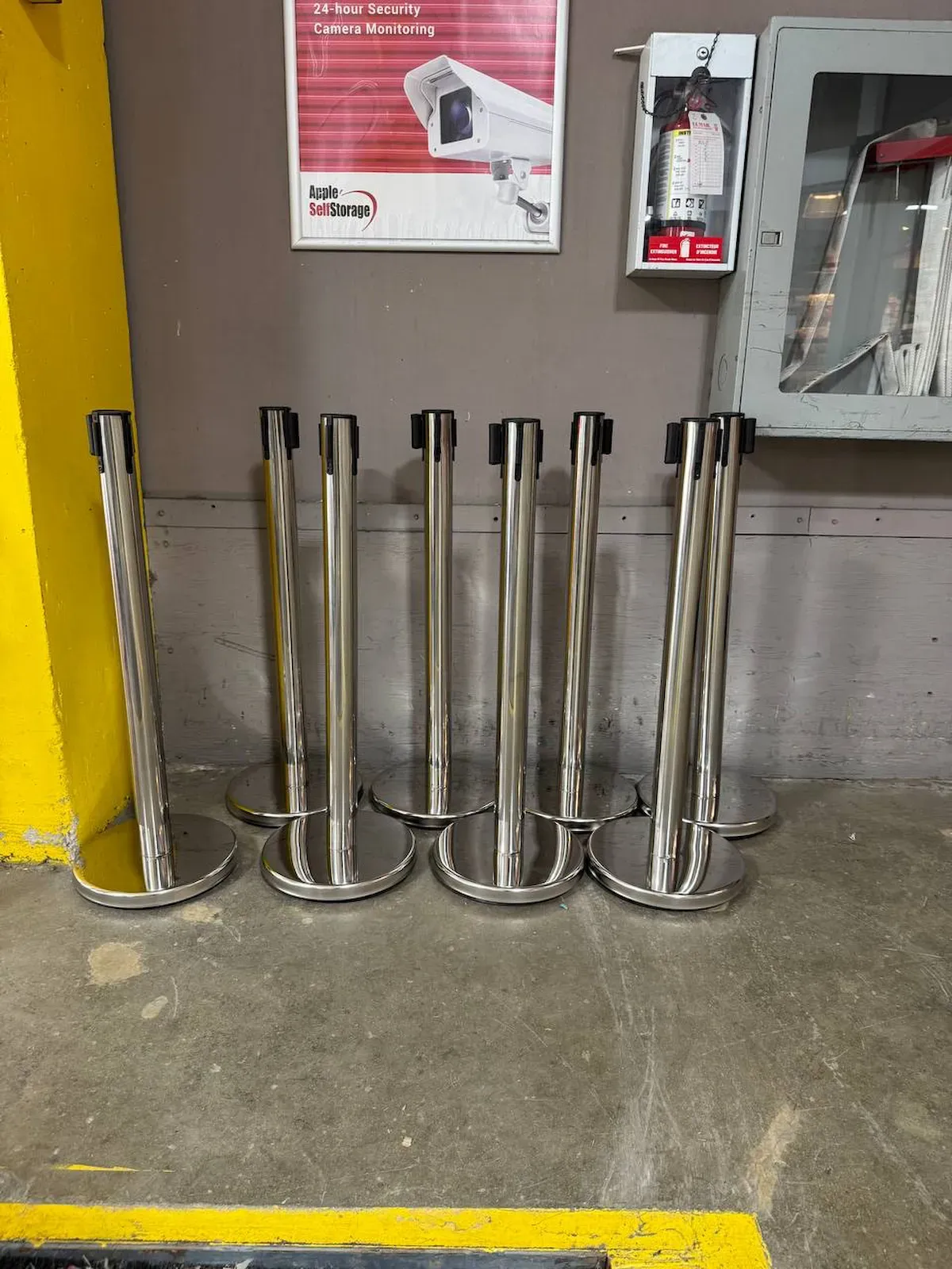 A row of polished chrome belt posts standing on a hard floor, the black belts run between them in a straight line
