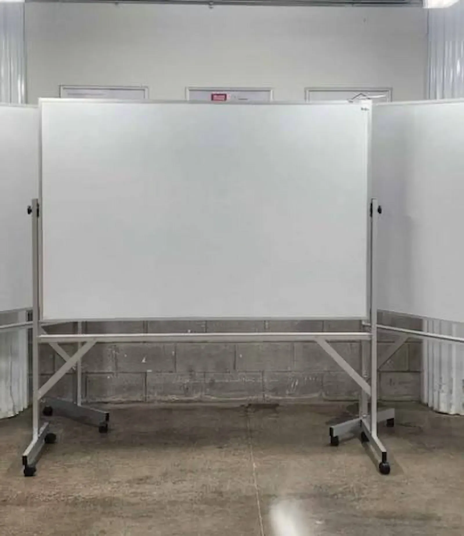 The same board standing on a concrete floor in a storage bay, wiped blank, its castors resting against the slab with white panelling behind it
