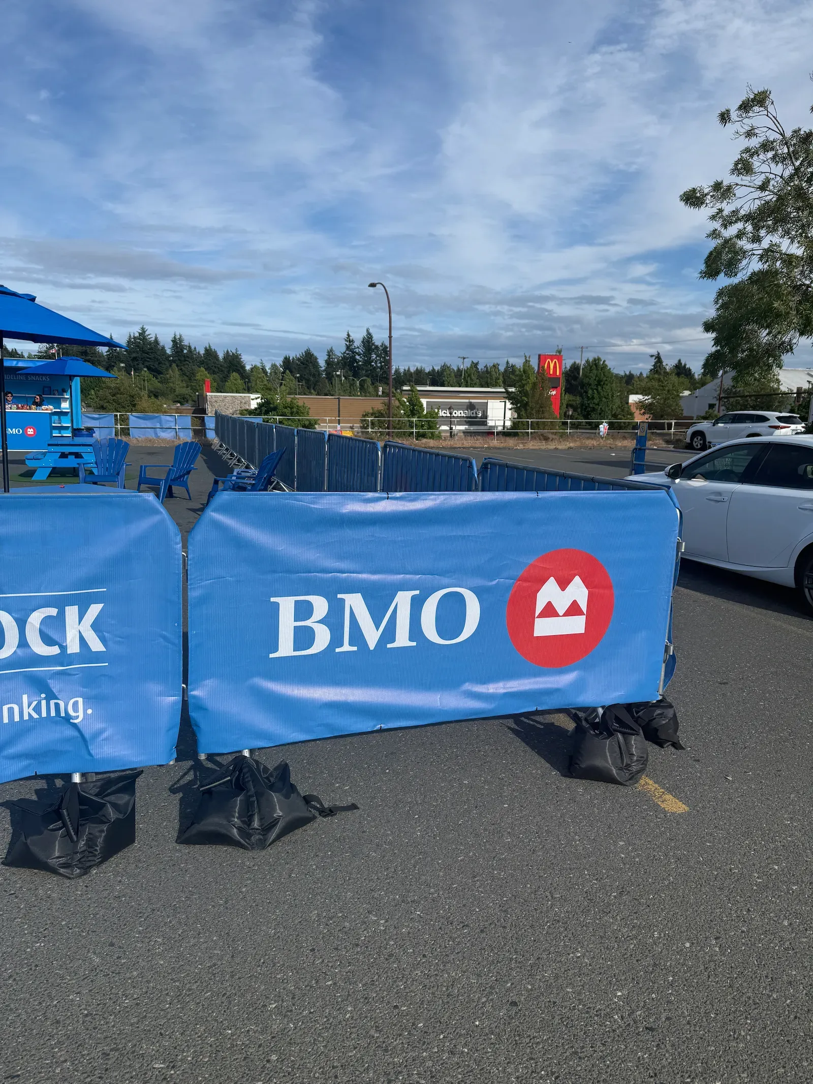Bike rack barricade sections dressed in blue BMO-branded covers, a black sandbag over every foot, closing off an outdoor site in a car park