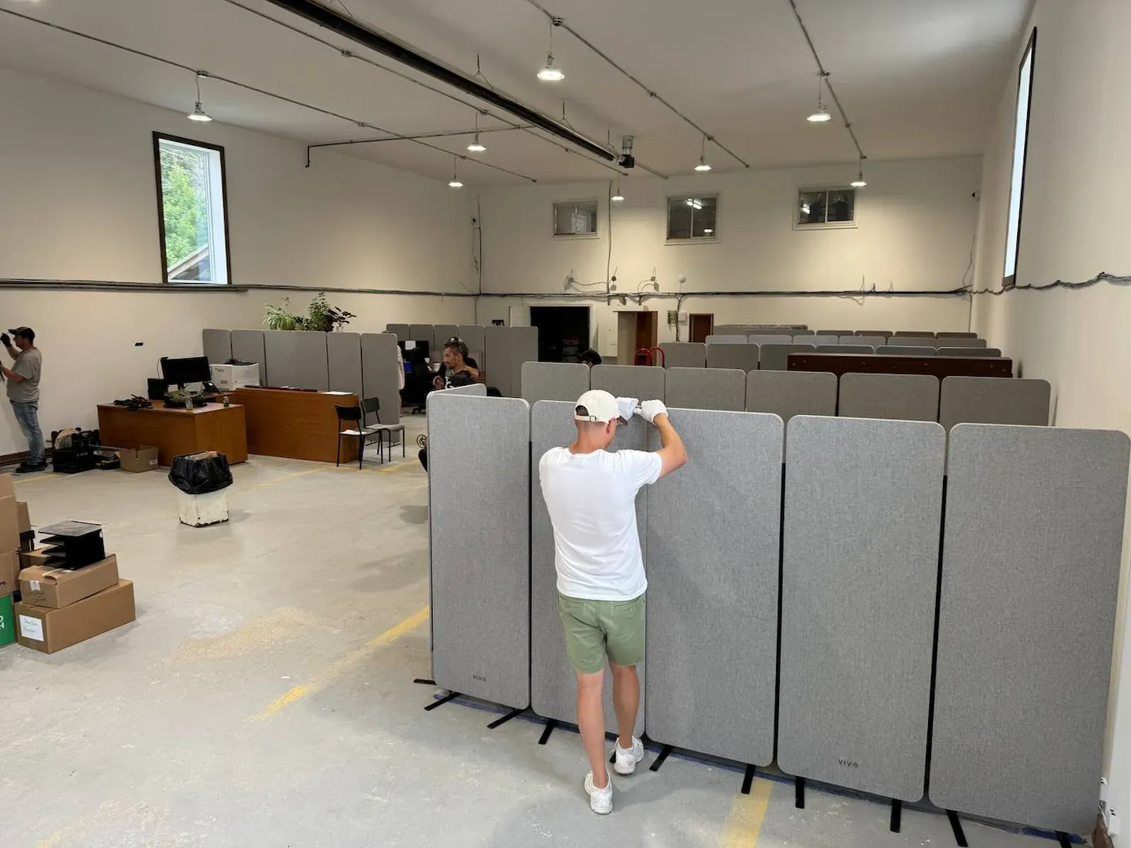 Grey acoustic privacy panels being lined up across the bare floor of an office fit-out, desks, stacked seating and packing boxes already in the room behind them