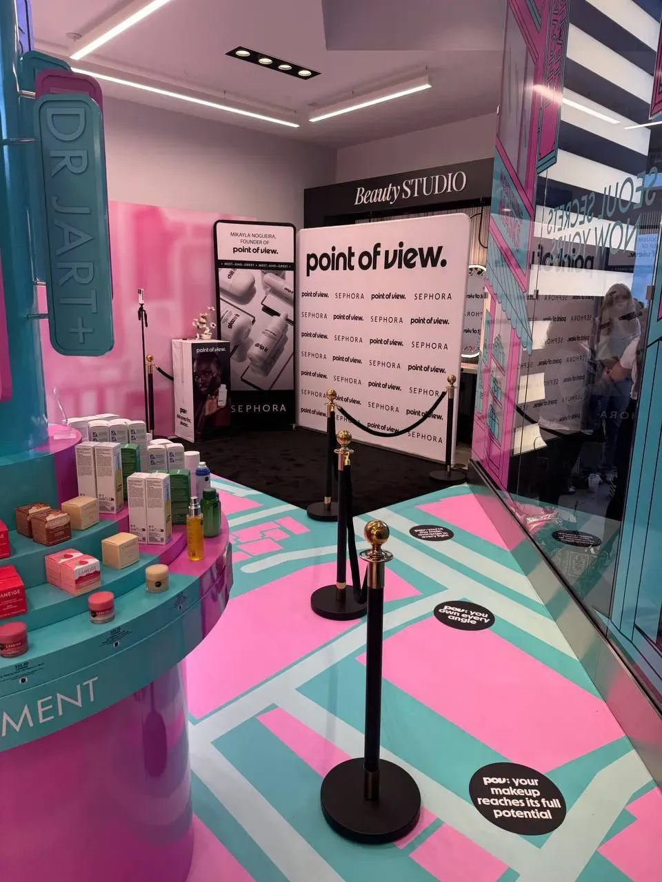 Black posts with gold ball tops and black ropes fencing off a photo wall on black carpet inside a cosmetics store