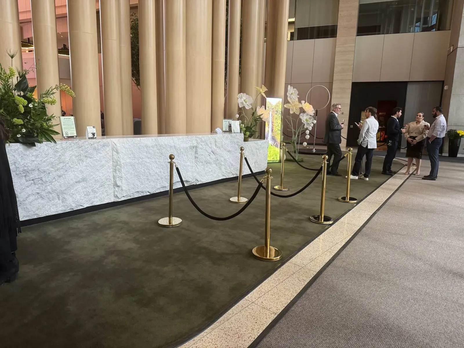 Gold posts and black ropes shaping a waiting line in front of a stone reception counter, guests standing beyond it