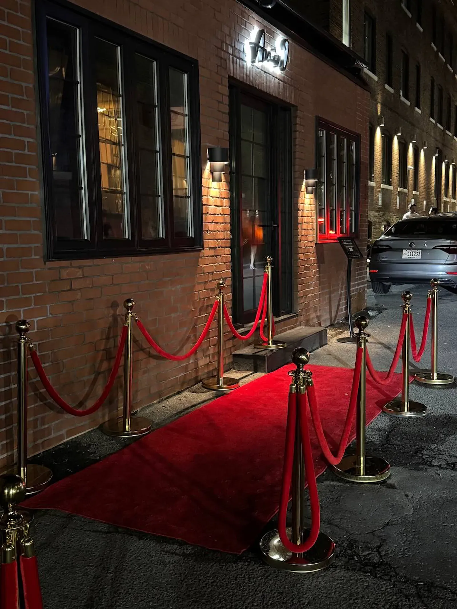 A red runner cut to the width of a doorway and taken out across the pavement to the kerb, posts down both edges