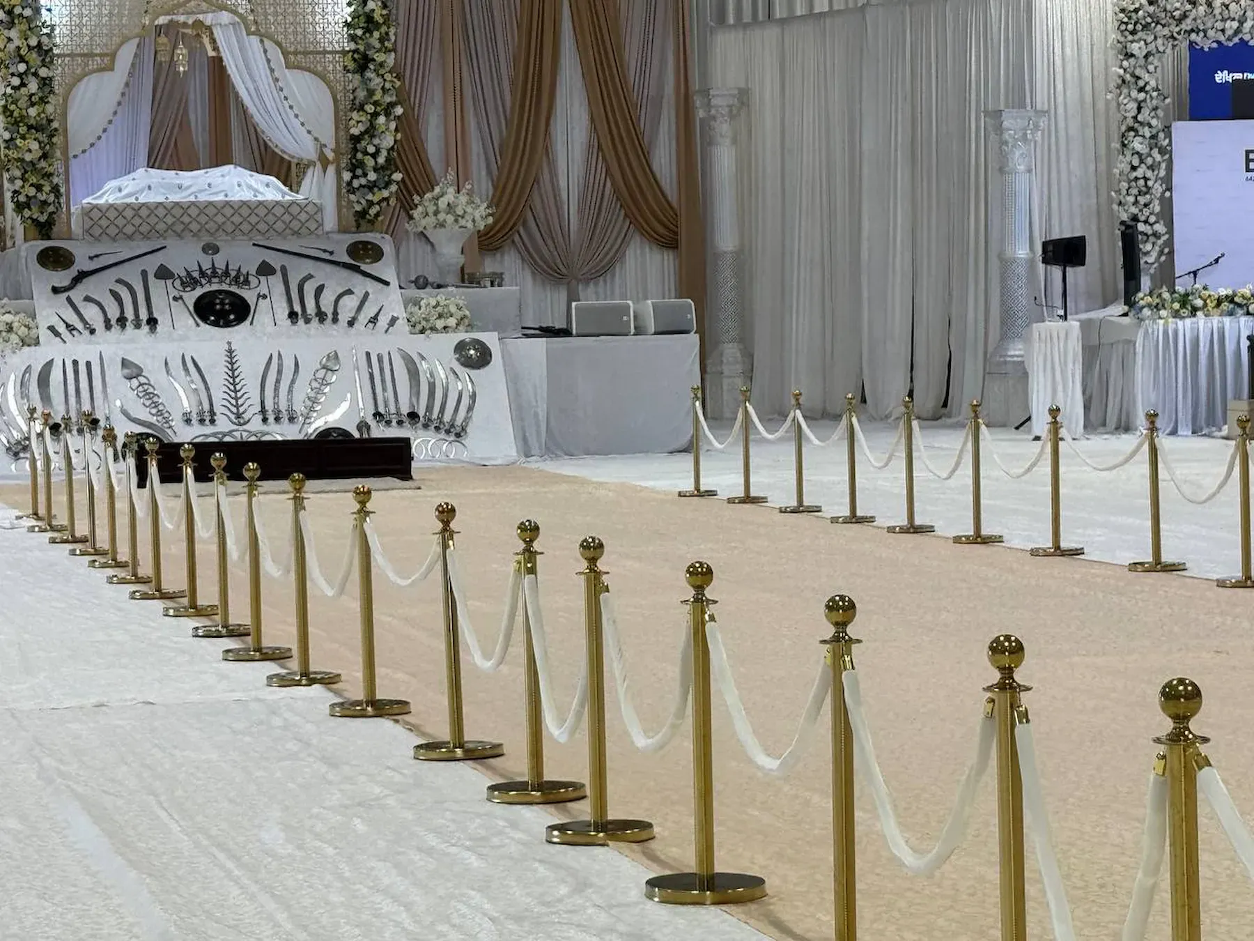Two long facing runs of gold posts and white ropes holding a ceremonial aisle open across a banquet floor
