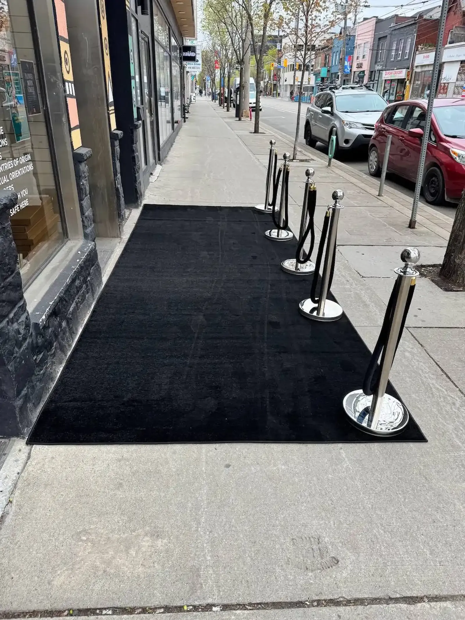 Chrome posts and black ropes standing along the street edge of a black runner outside a shopfront